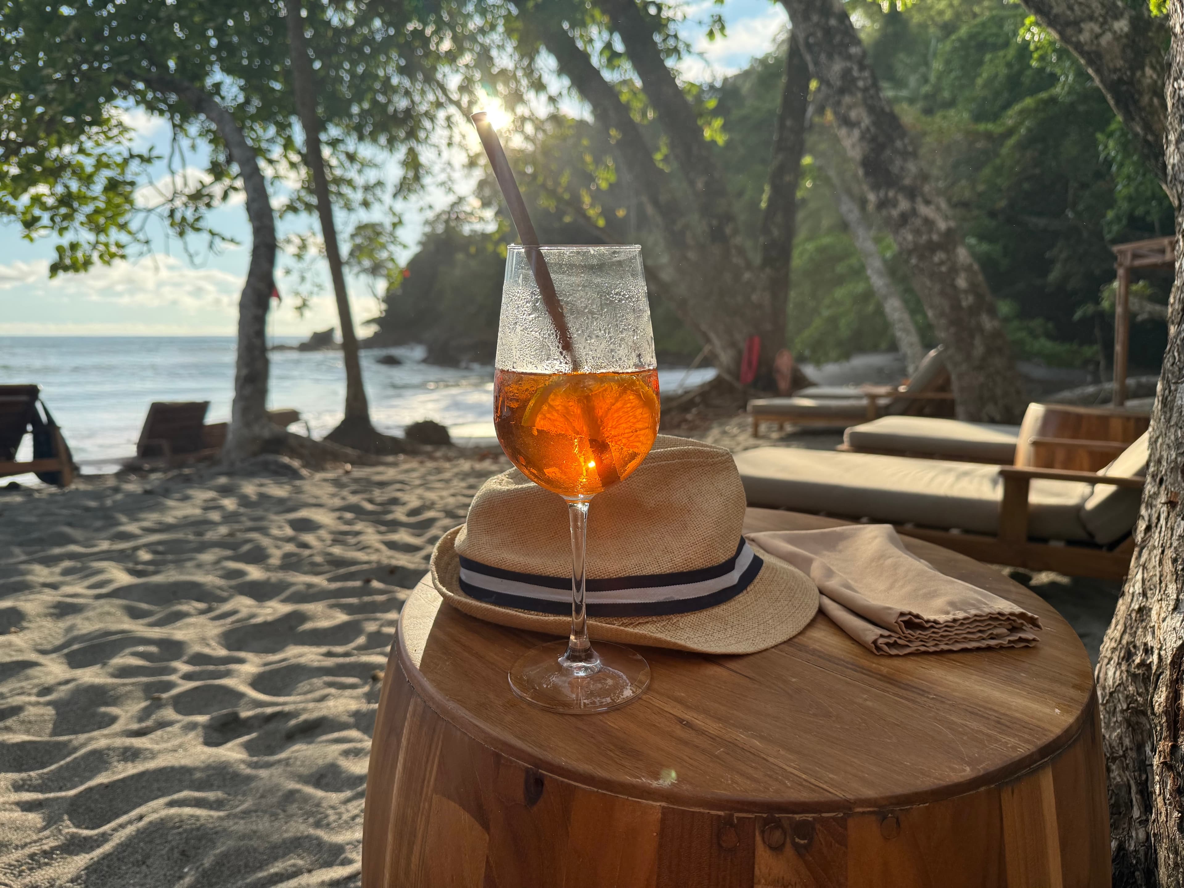 A cocktail and a straw hat on a table on a jungle-lined beach