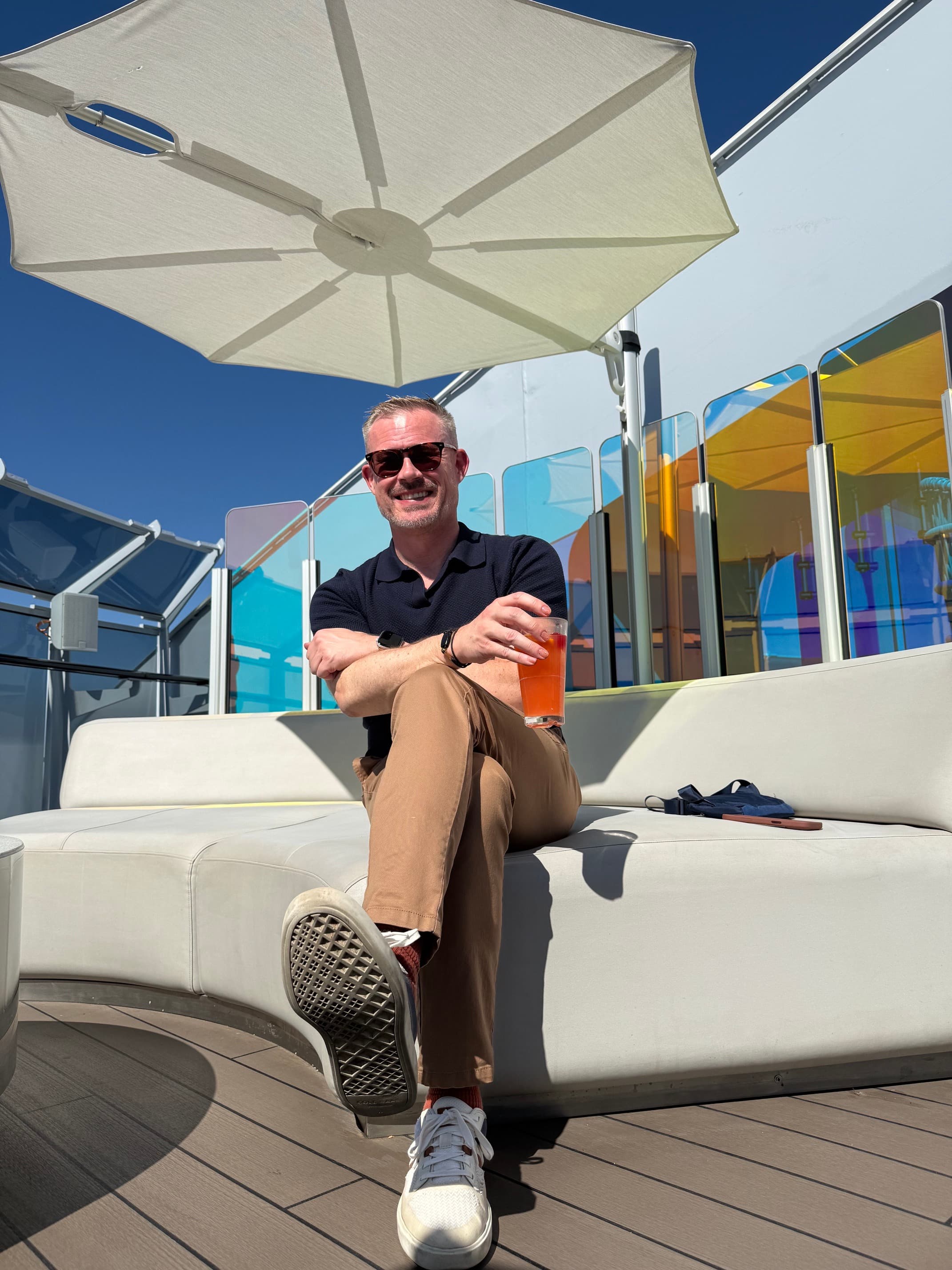 Kyle with a drink in hand on a sunny cruise ship deck, watching the water